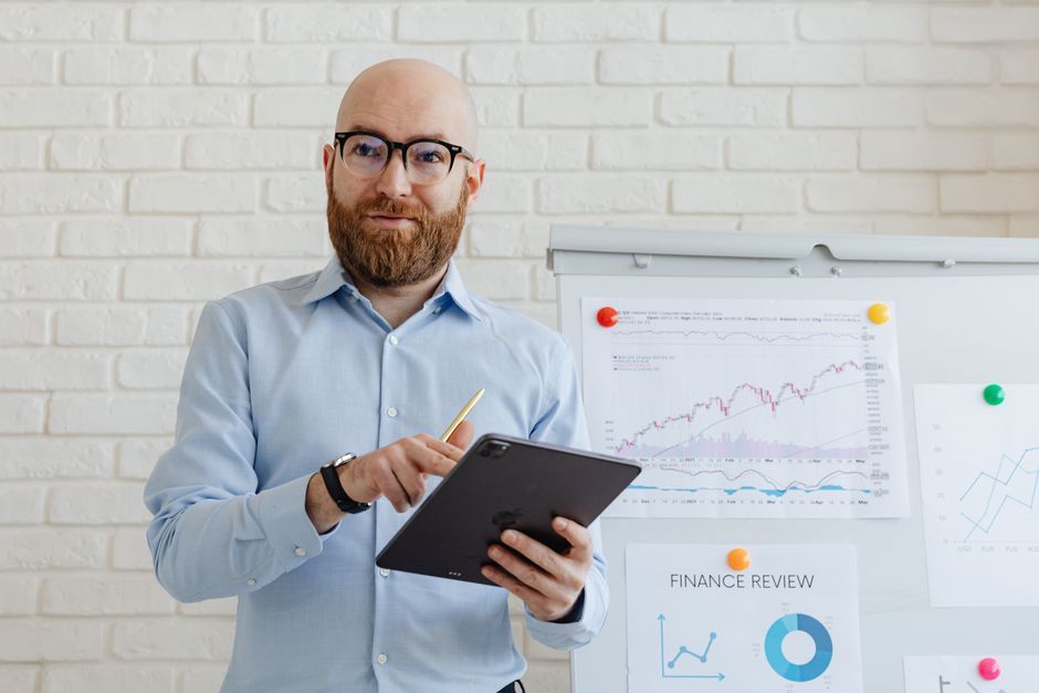 Businessman presenting data analysis on whiteboard, holding tablet, in modern office.