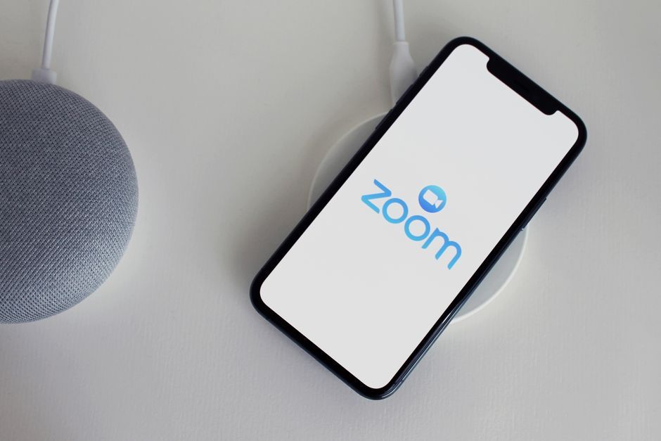 Close-up of a smartphone with Zoom app on a wireless charger next to a smart speaker.
