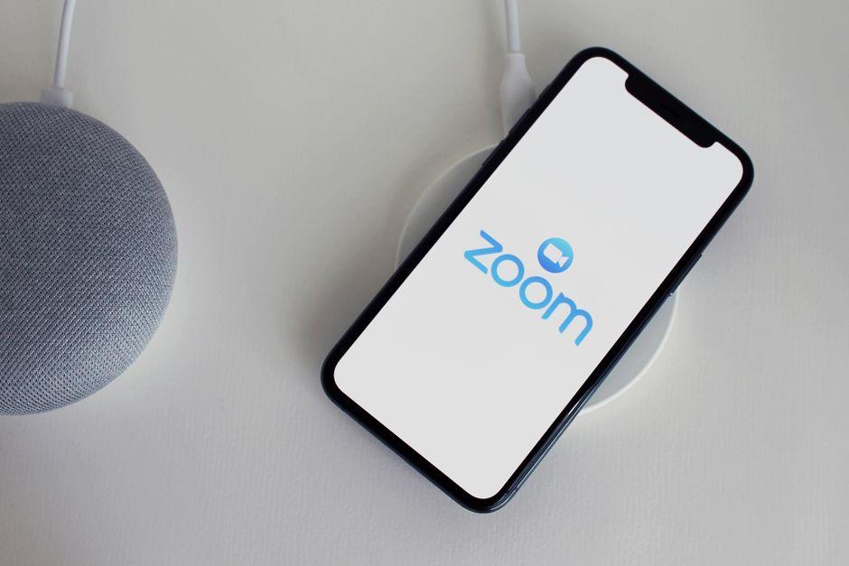 Close-up of a smartphone with Zoom app on a wireless charger next to a smart speaker.