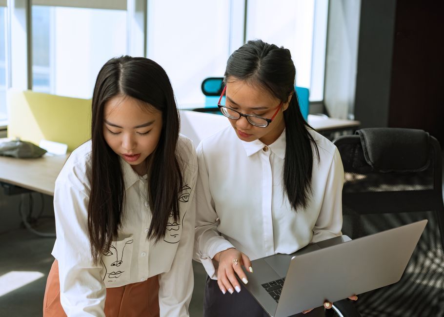 Two women engaged in discussion over work documents in a modern office setting.